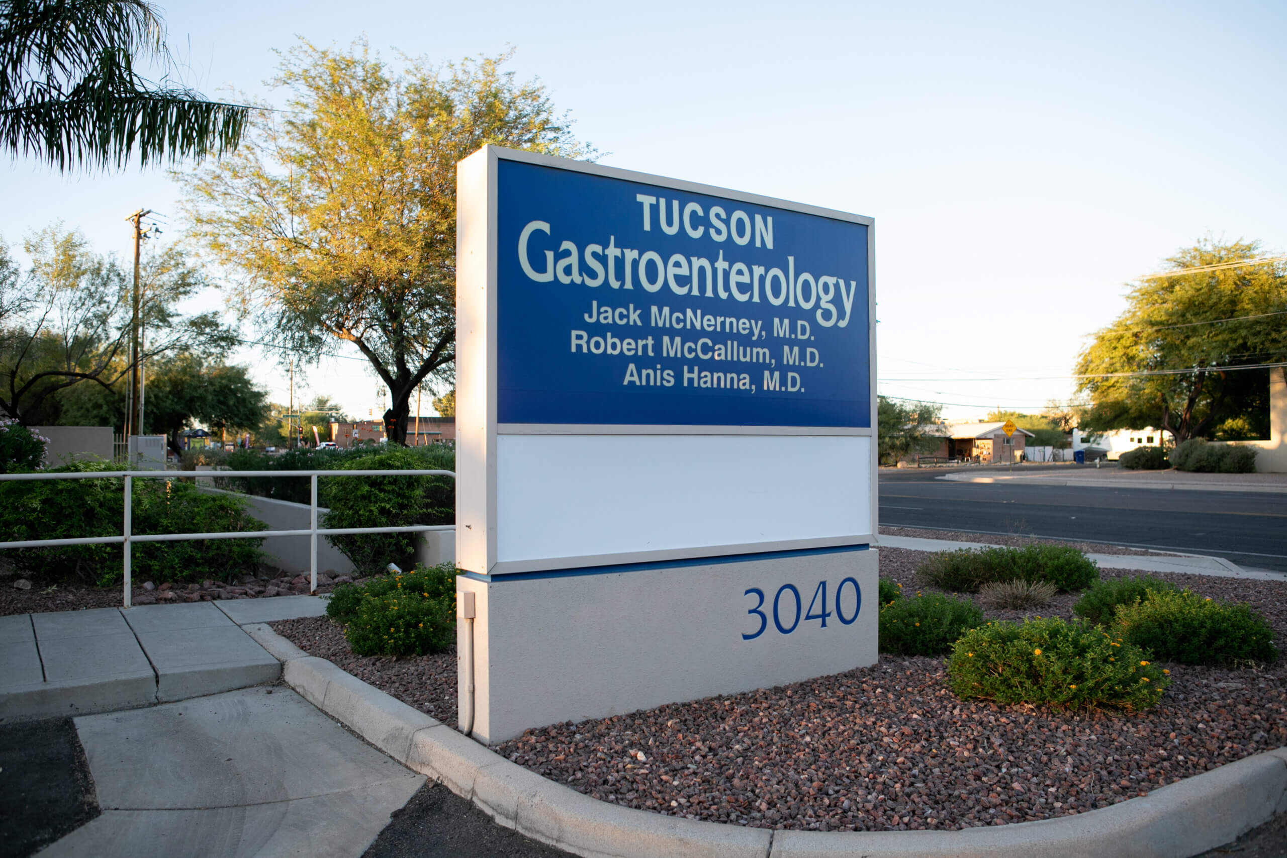 A large blue and white sign in the garden at the entrance to Tucson Gastroenterology Specialists detailing information about the digestive specialists